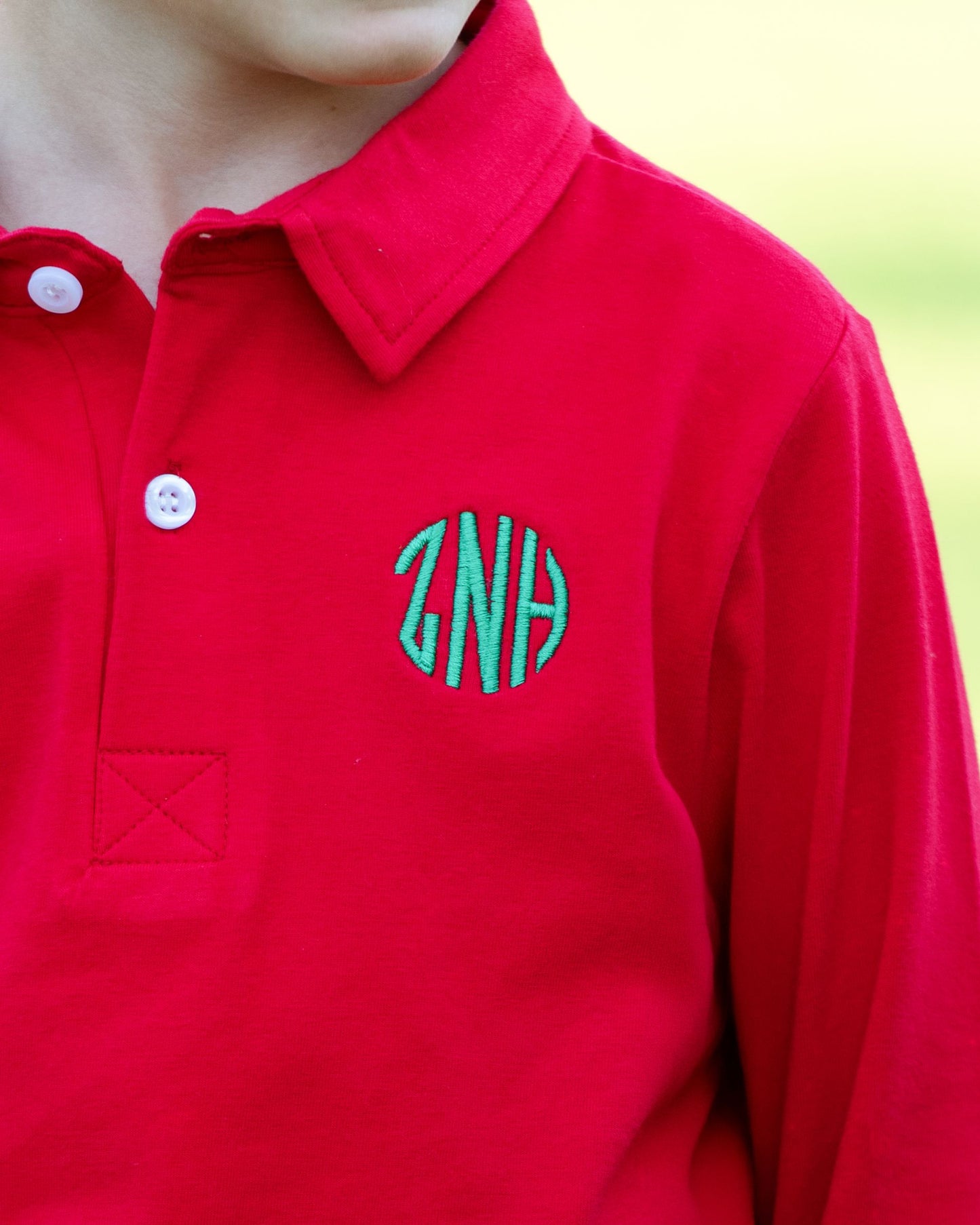 Red polo shirt with green monogram on a blurred background