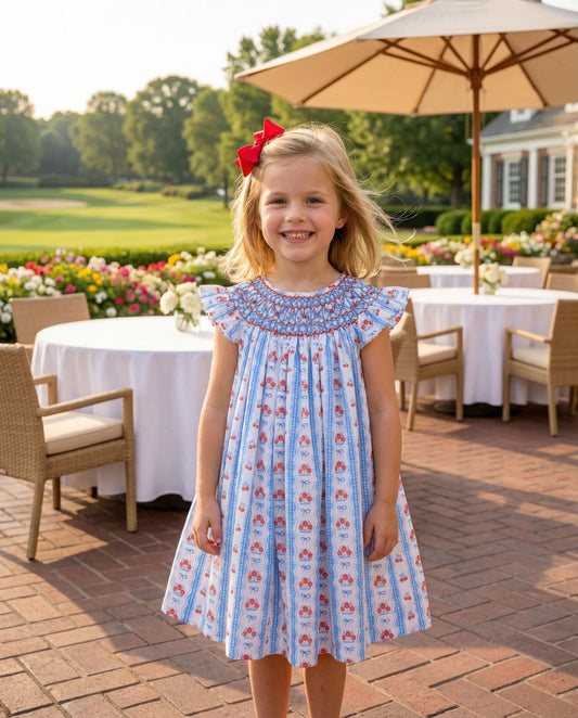 Smiling girl in a blue and red dress with smocking details on the neckline.