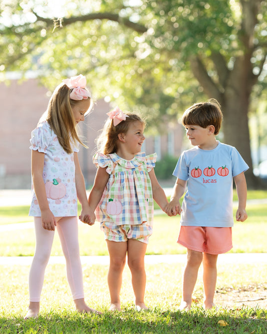 Three children holding hands in a park with pumpkin outfits on a sunny day