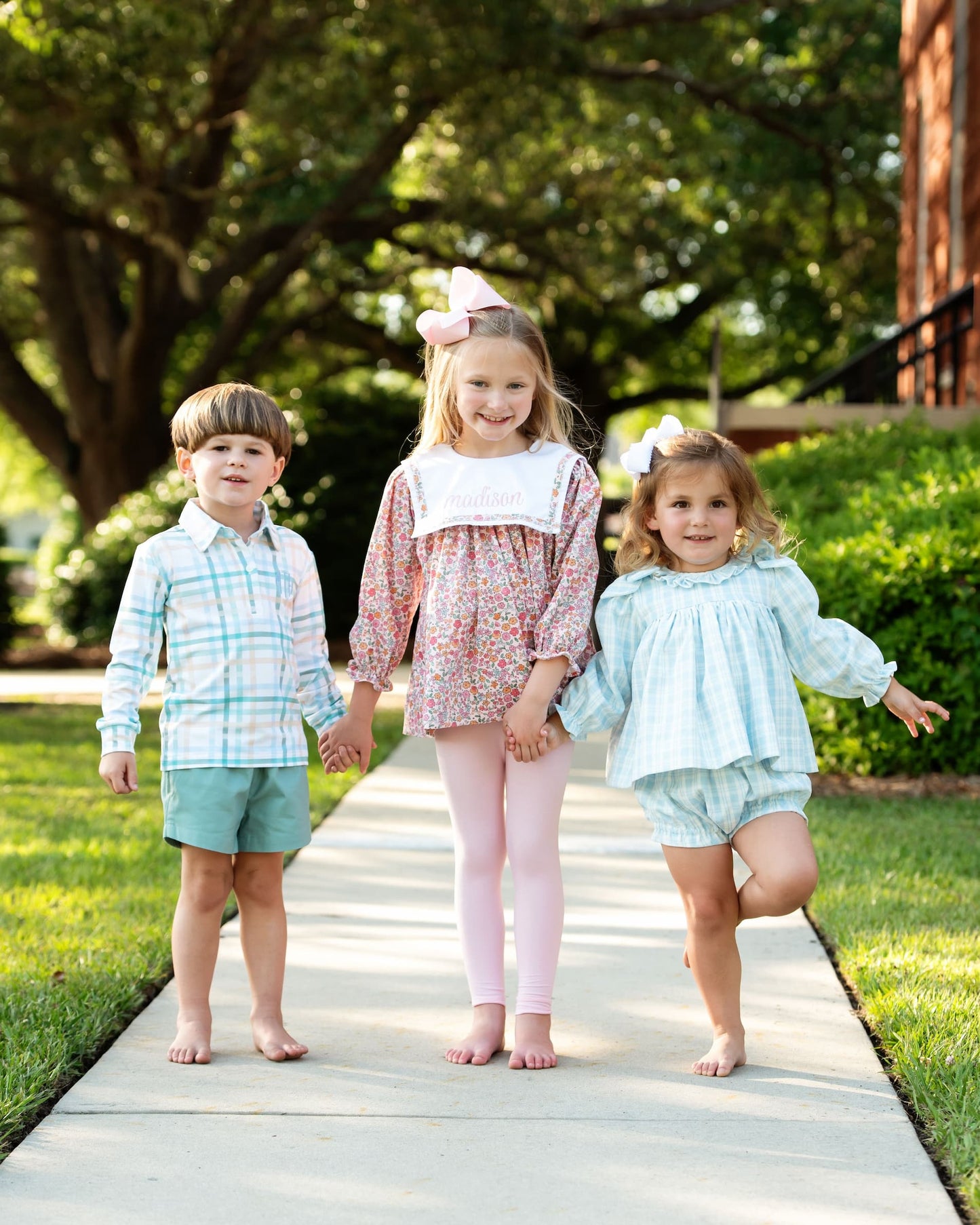 Three children holding hands on a wooden path with greenery in the background