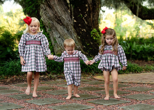 Three children in matching plaid outfits walking hand-in-hand on a stone path.