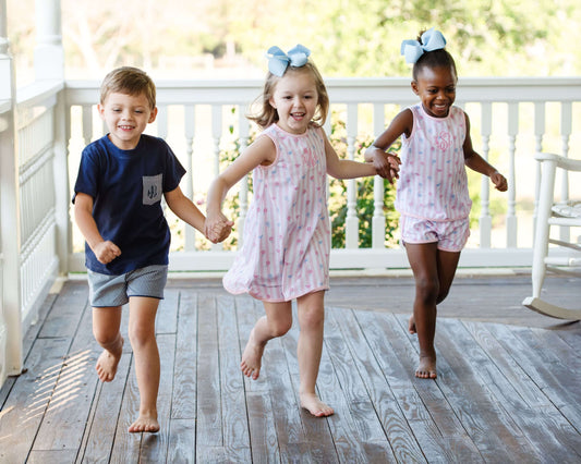 Three children running on a wooden deck holding hands with a white railing.