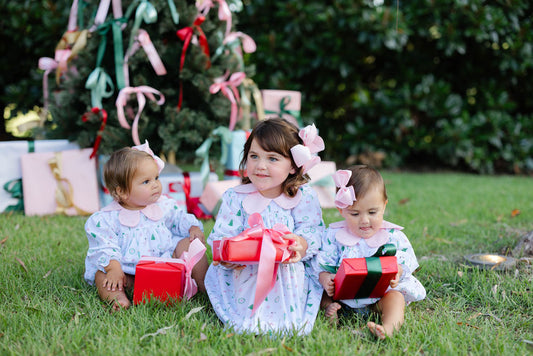 Three children sitting on grass with Christmas presents and decorations in the background.