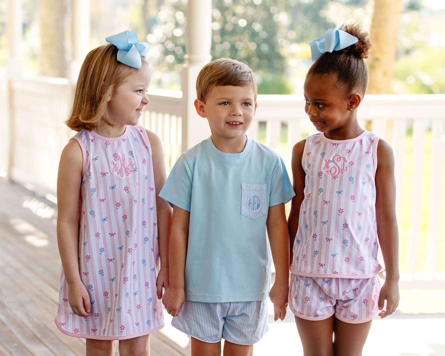 Three children wearing spring outfits on a wooden deck.