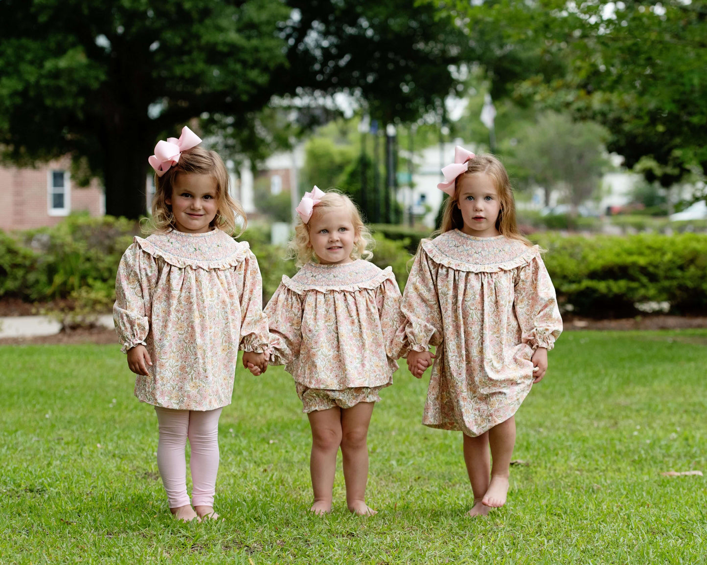 Three young girls in matching dresses standing on grass with trees in the background