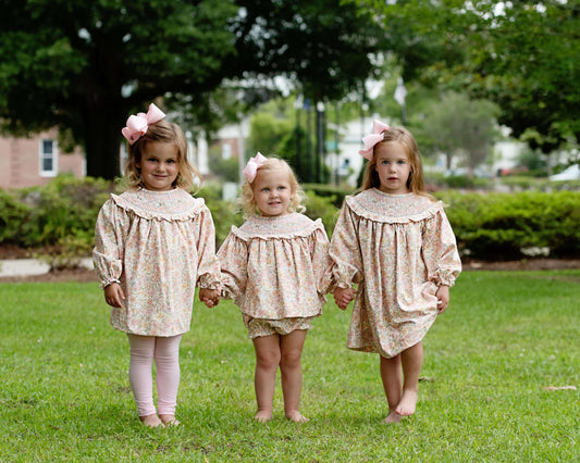 Three young girls in matching dresses standing on grass with trees in the background