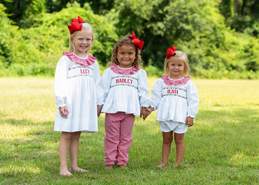 Three young girls in matching outfits with name labels standing in a grassy field.