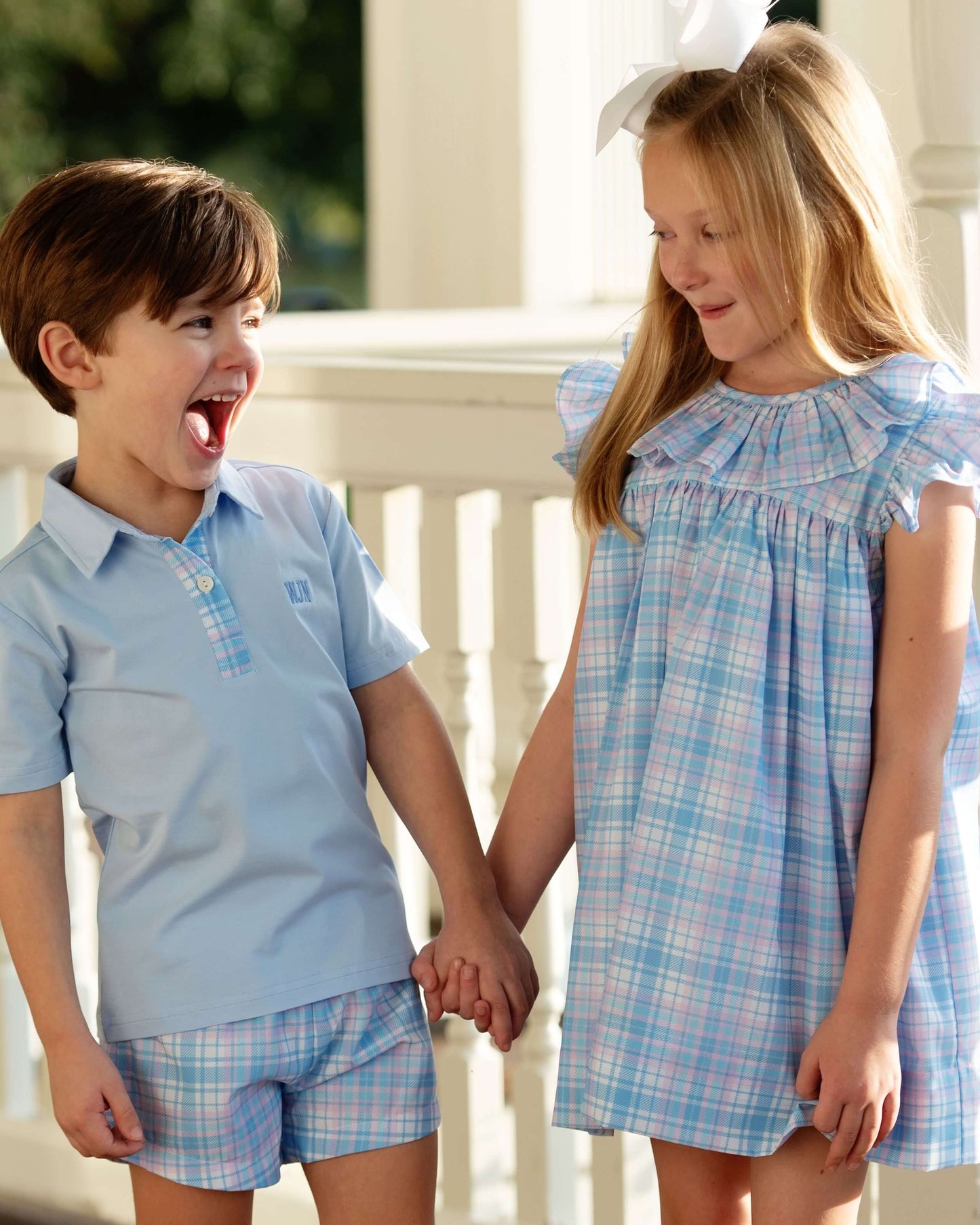Two children, a boy and a girl, holding hands and smiling outdoors.