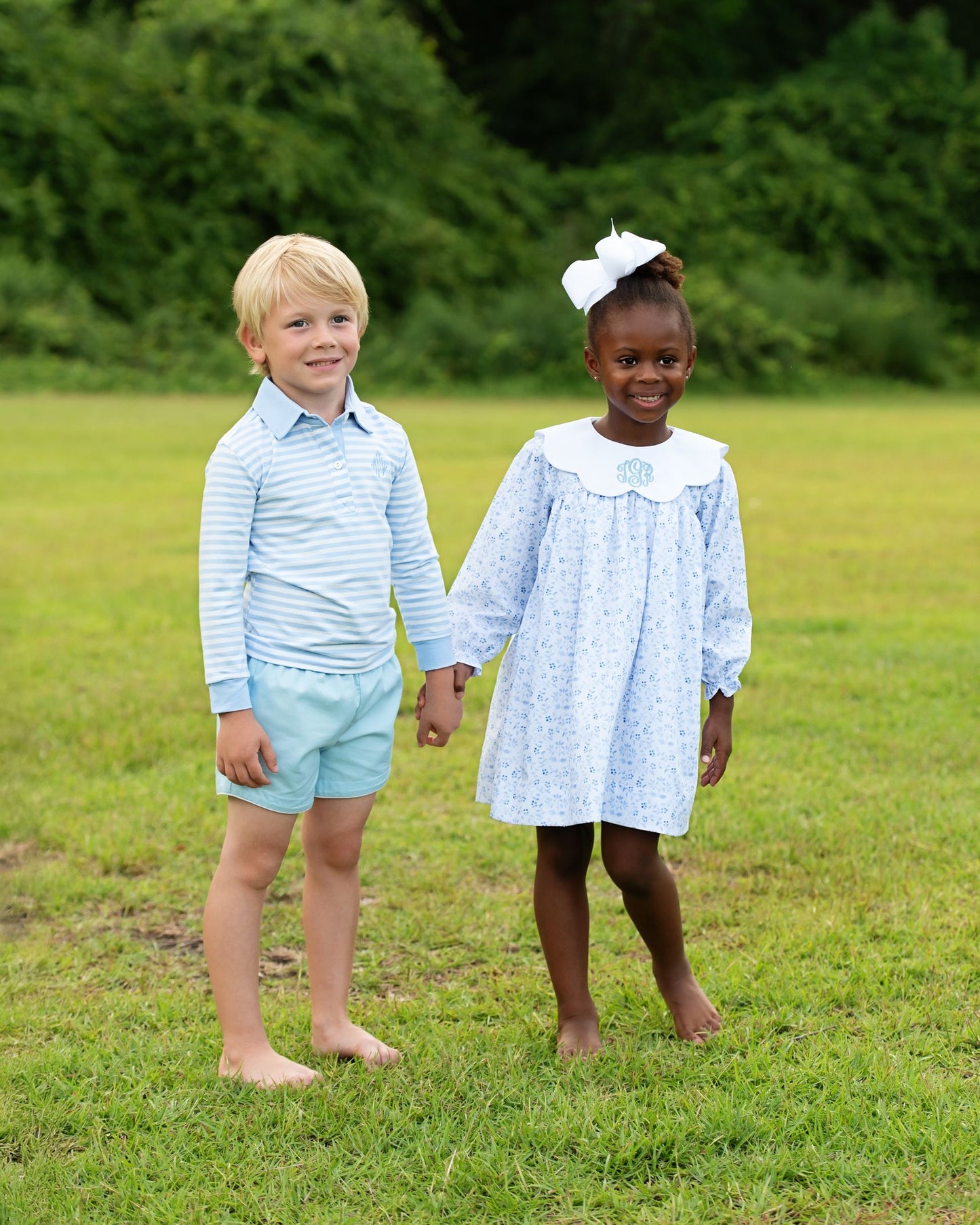 Two children, a boy and a girl, standing in a grassy field holding hands.