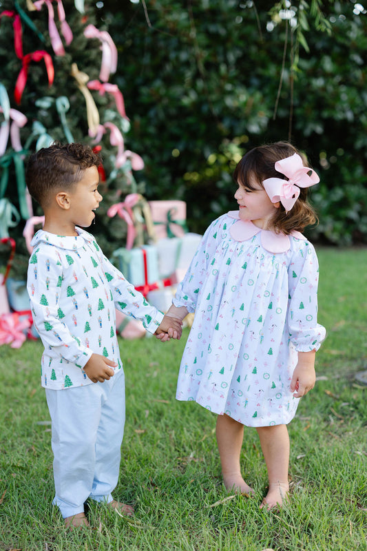 Two children, a boy and a girl, standing outdoors with a decorated Christmas tree in the background.