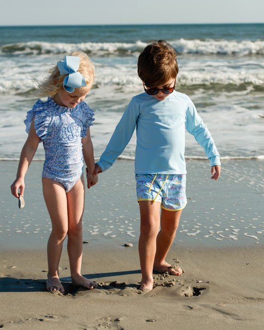 Two children holding hands on a beach with ocean waves in the background.