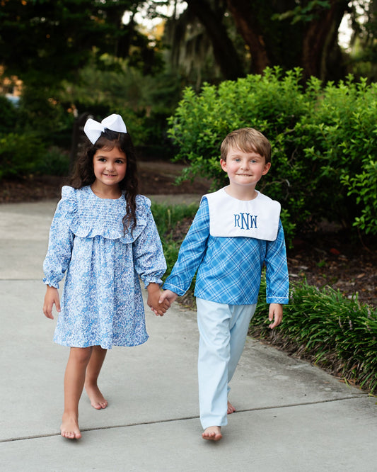 Two children holding hands on a sidewalk with greenery in the background
