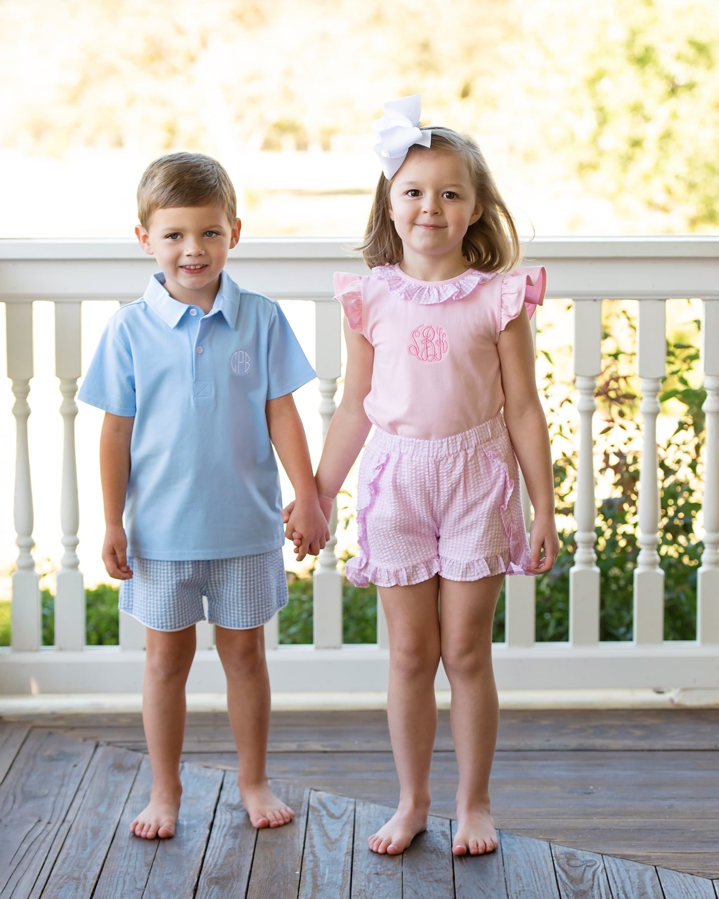 Two children holding hands on a wooden deck, wearing matching seersucker outfits.