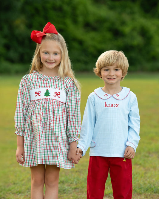 Two children holding hands outdoors, one in a dress with a tree design and the other in a light blue shirt with 'knox' printed on it.