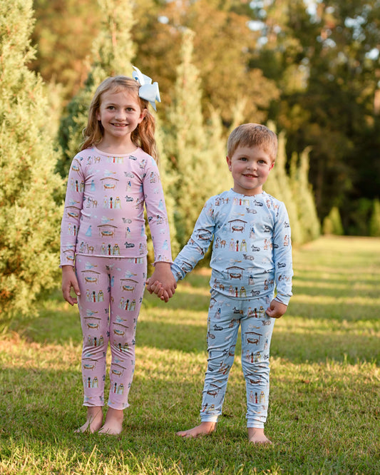 Two children holding hands outdoors wearing pajamas with vehicle patterns.