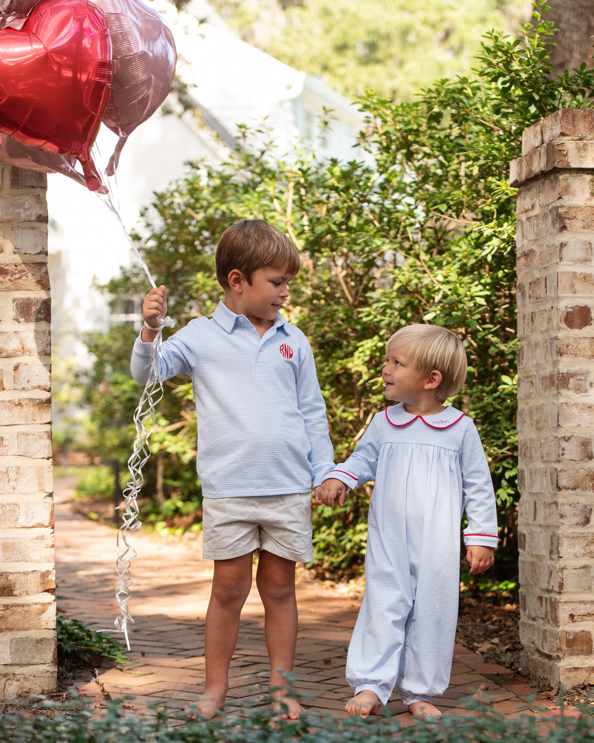 Two children holding hands outdoors with a heart-shaped balloon.