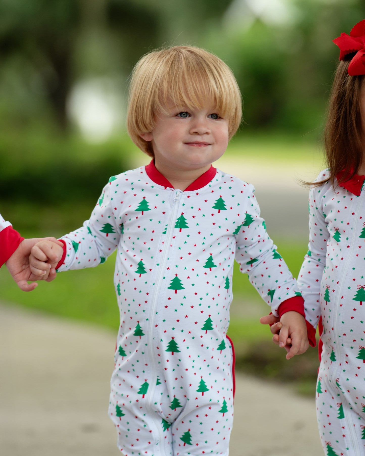 Two children in matching Christmas-themed pajamas holding hands outdoors.
