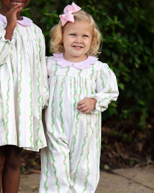 Two children in matching dresses with green patterns standing outdoors.