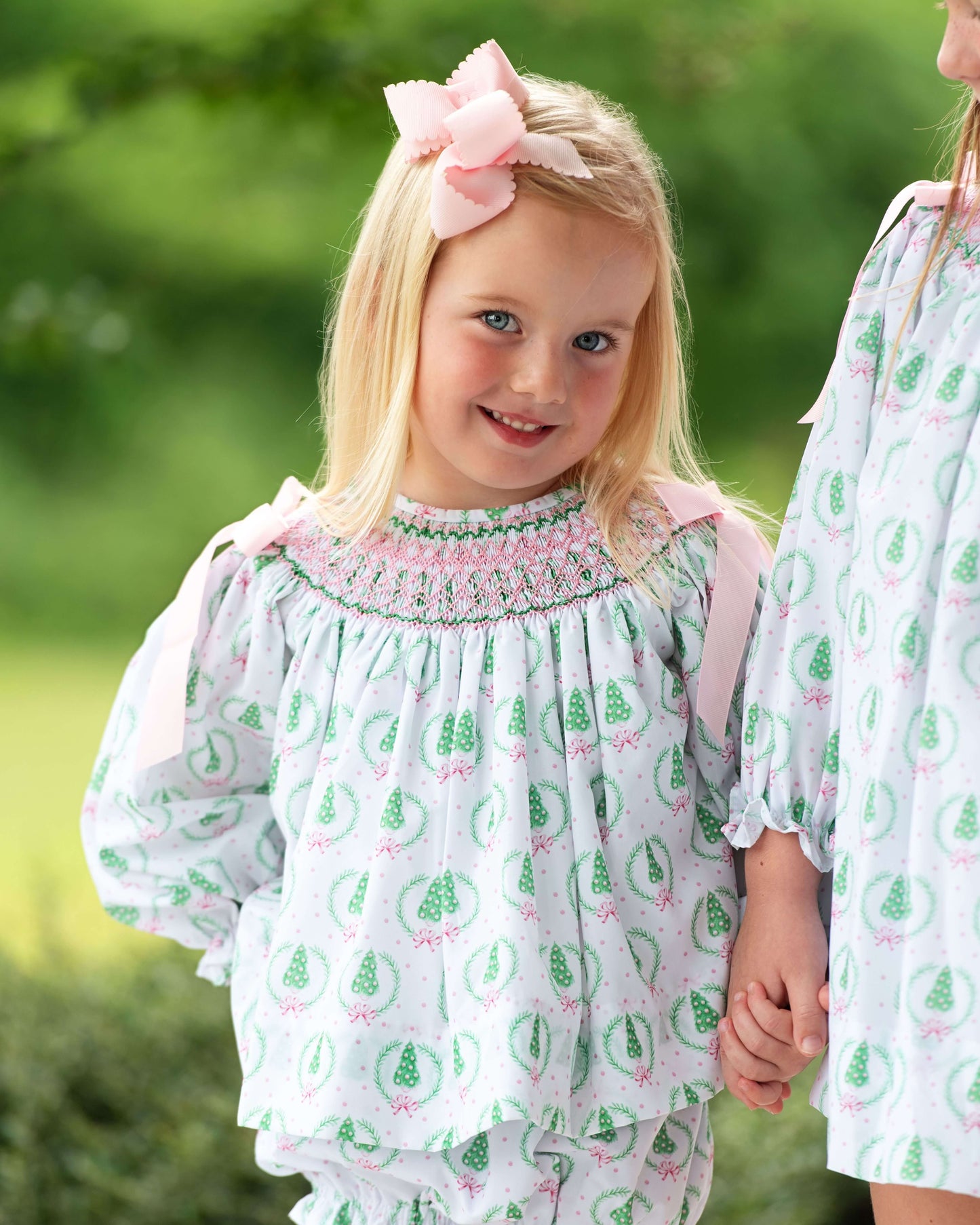 Two children in matching green and white outfits with a blurred natural background