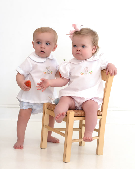 Two children in matching outfits sitting on a chair against a white background