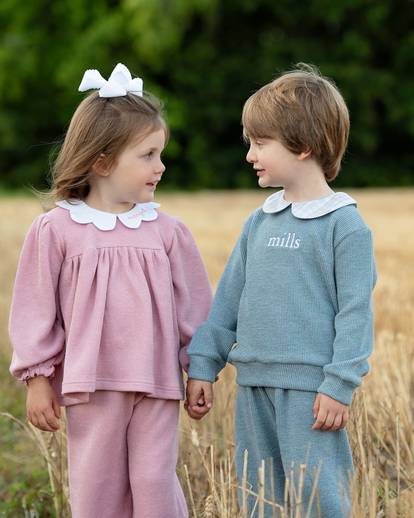 Two children in matching outfits standing in a field.