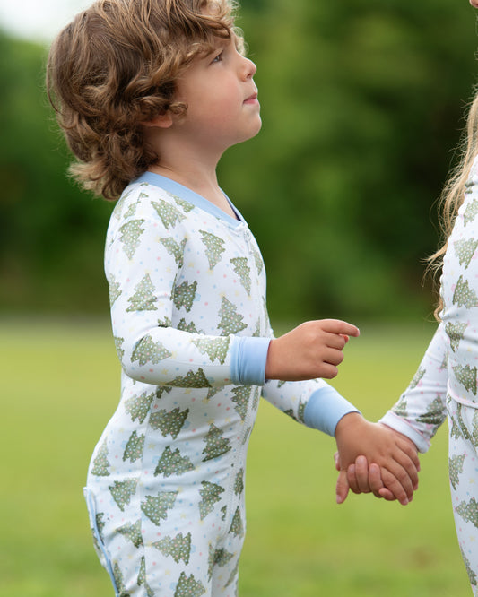 Two children in matching outfits standing outdoors with a blurred green background