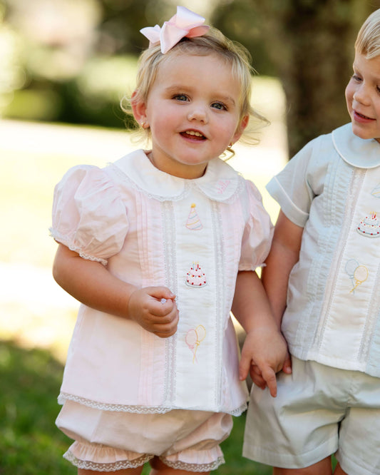 Two children in matching outfits standing outdoors with a blurred natural background