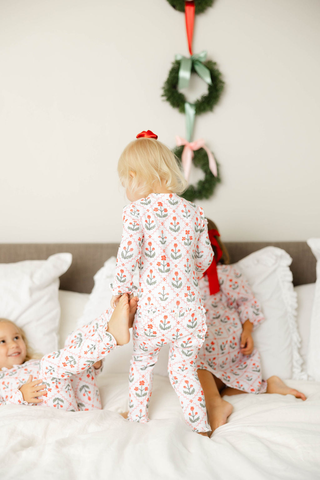 Two children in matching pajamas sitting on a bed with Christmas decorations in the background.