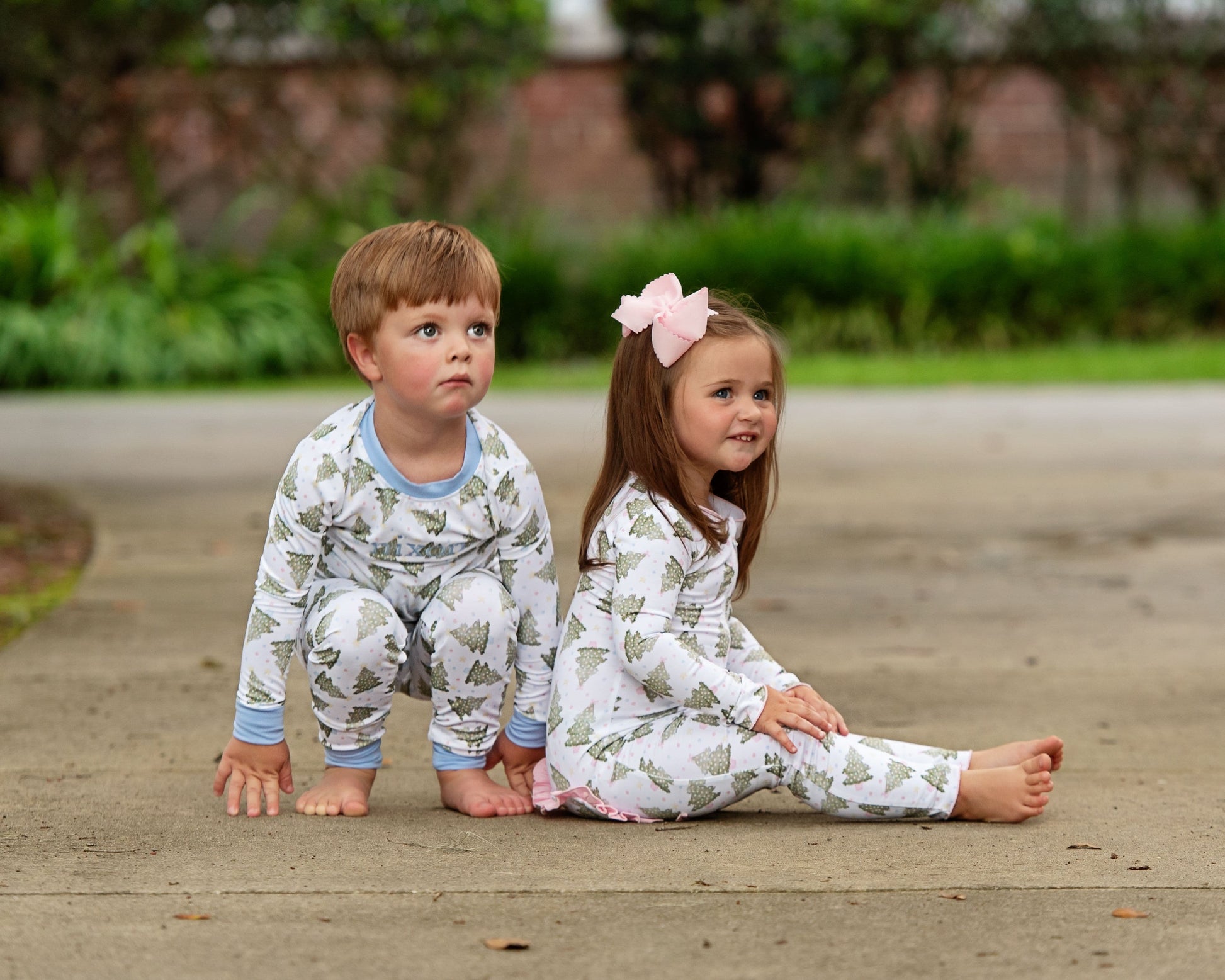 Two children in matching pajamas sitting on a path outdoors.