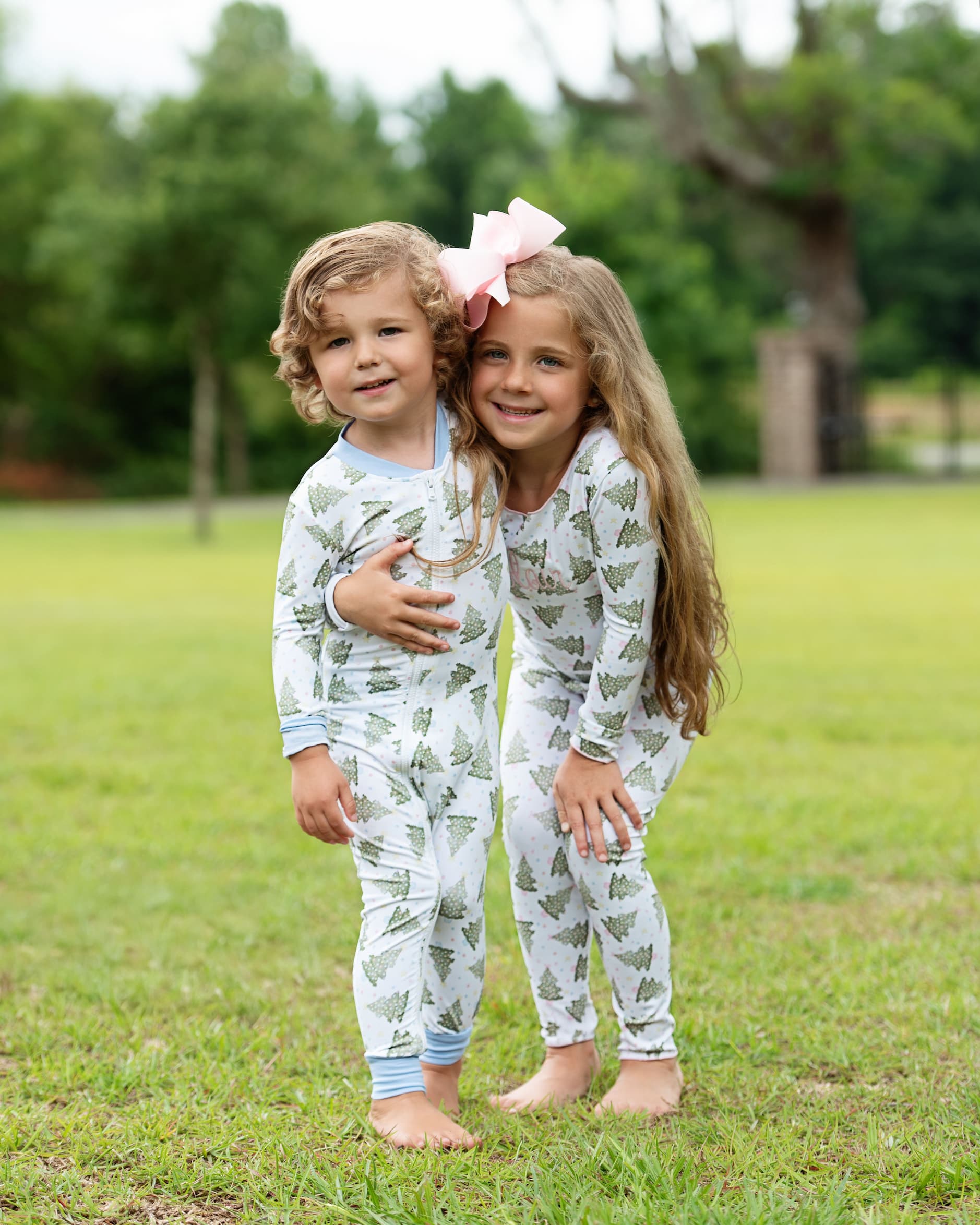 Two children in matching pajamas standing on grass with trees in the background