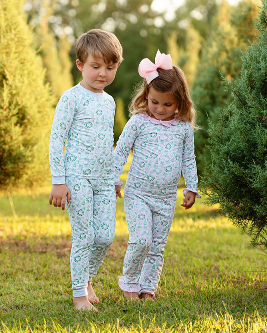 Two children in matching pajamas standing outdoors in a grassy area with trees.