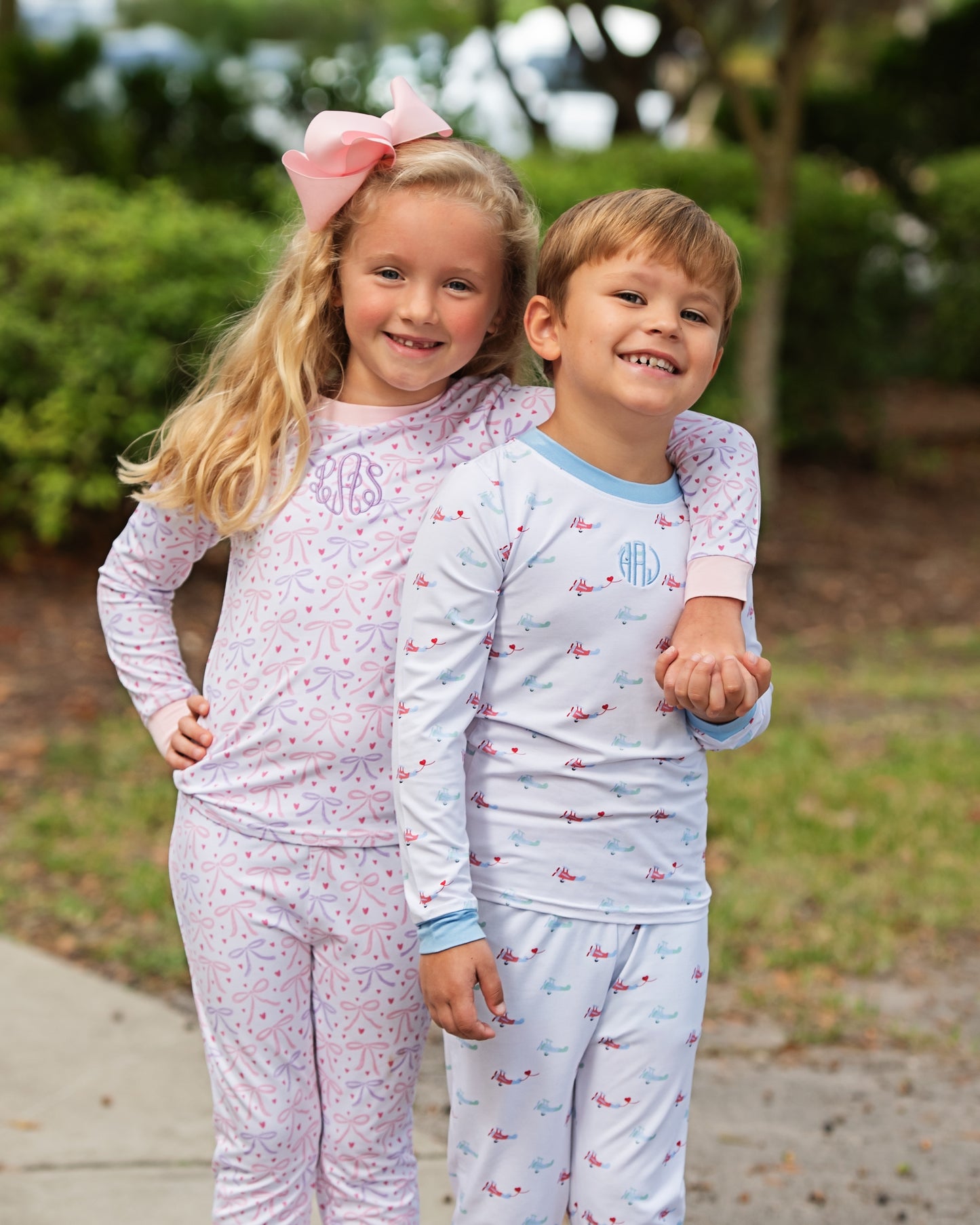 Two children in matching pajamas standing outdoors with a blurred background