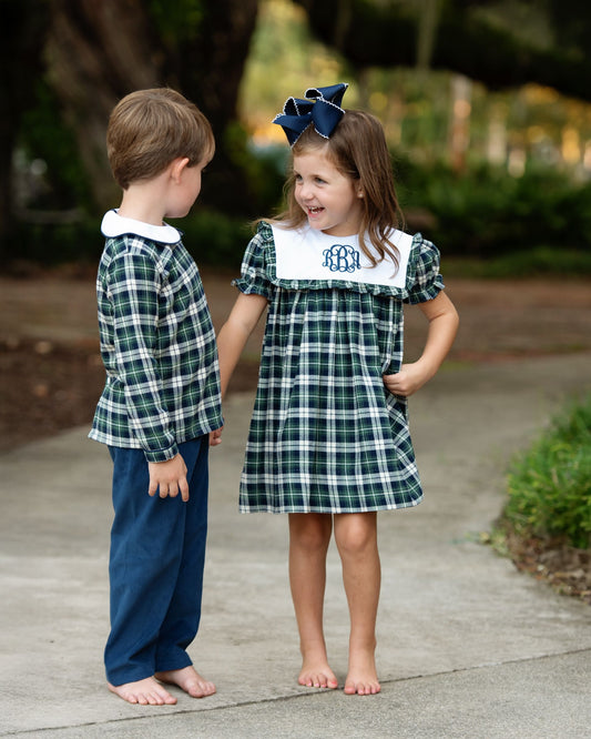 Two children in matching plaid outfits standing on a sidewalk.