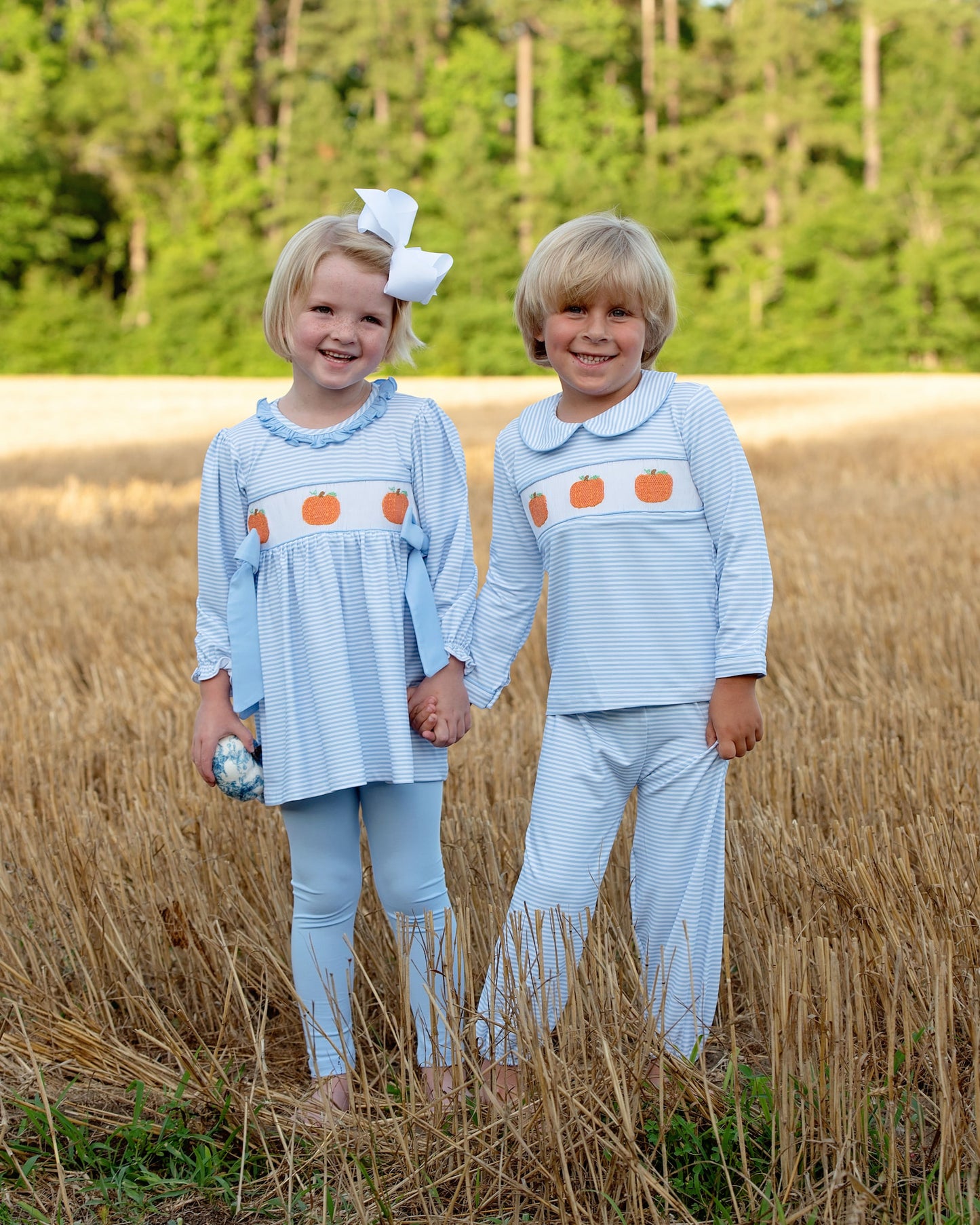 Two children in matching pumpkin outfits standing in a field with trees in the background