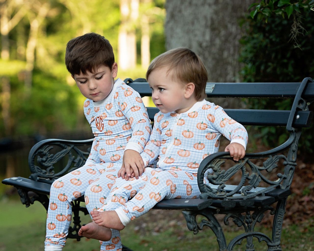 Two children in matching pumpkin pajamas sitting on a bench outdoors