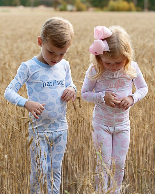 Two children in matching pumpkin set standing in a field.