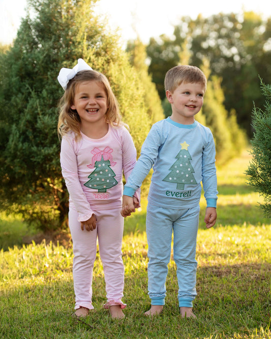 Two children in pajamas standing outdoors with a blurred background of trees and grass.
