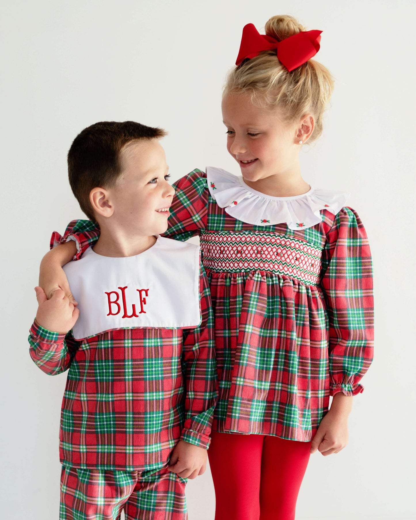 Two children in red and green plaid outfits with a white bib and red bow.