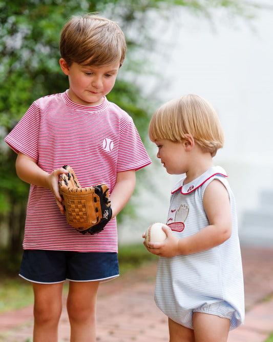 Two children outdoors, one holding a baseball glove and the other a baseball.