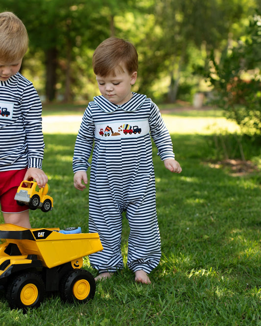 Two children playing with toy trucks in a grassy outdoor area.