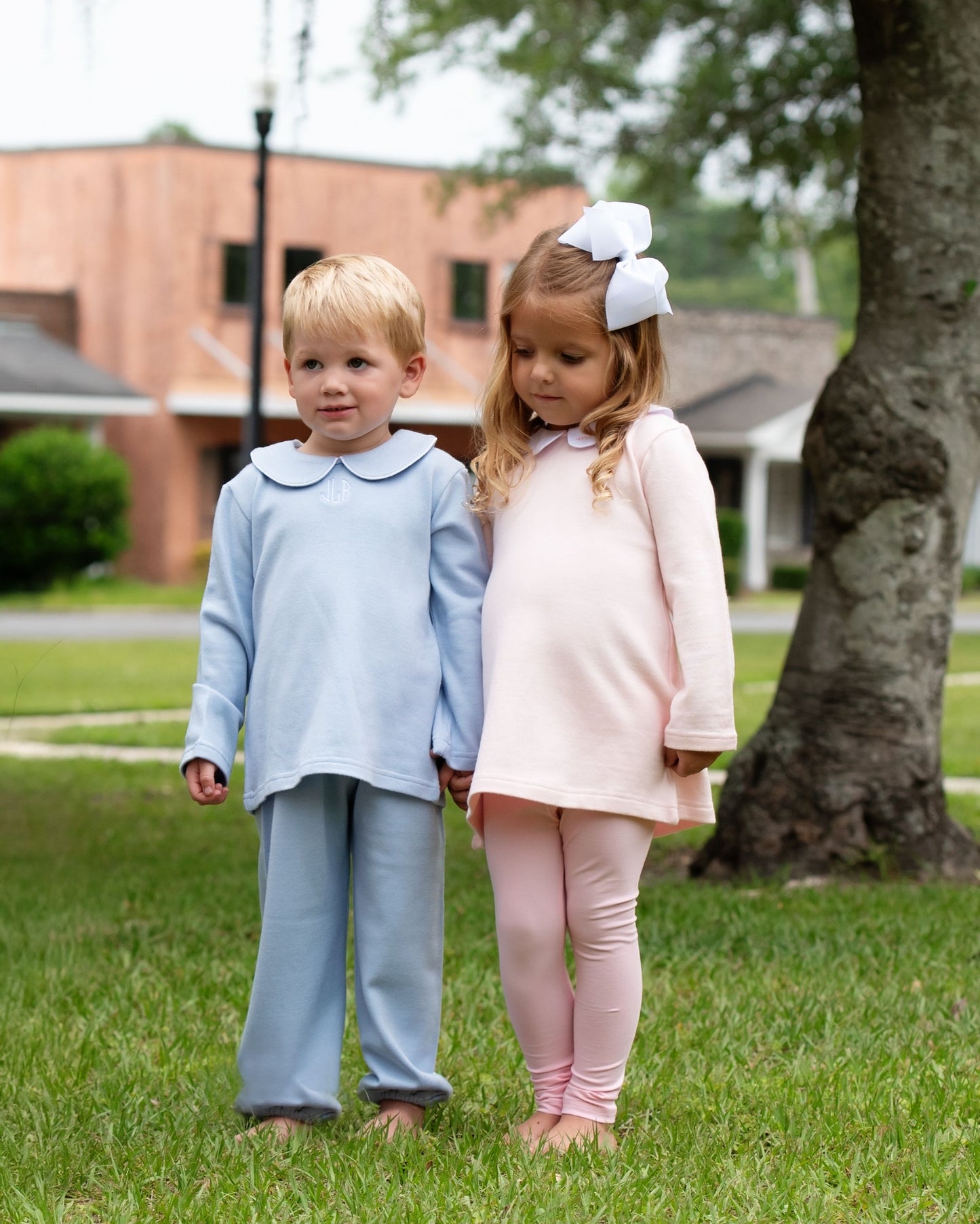 Two children standing outdoors on grass with a building in the background