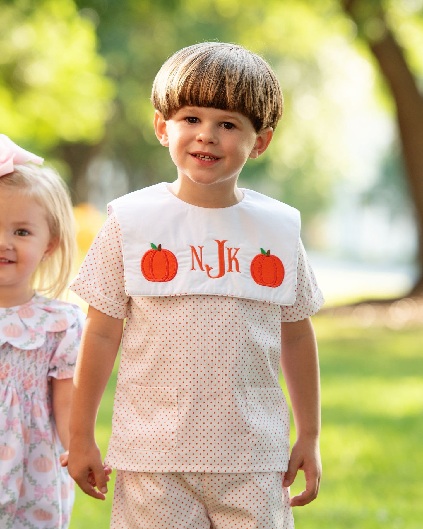 Two children standing outdoors with pumpkin outfits