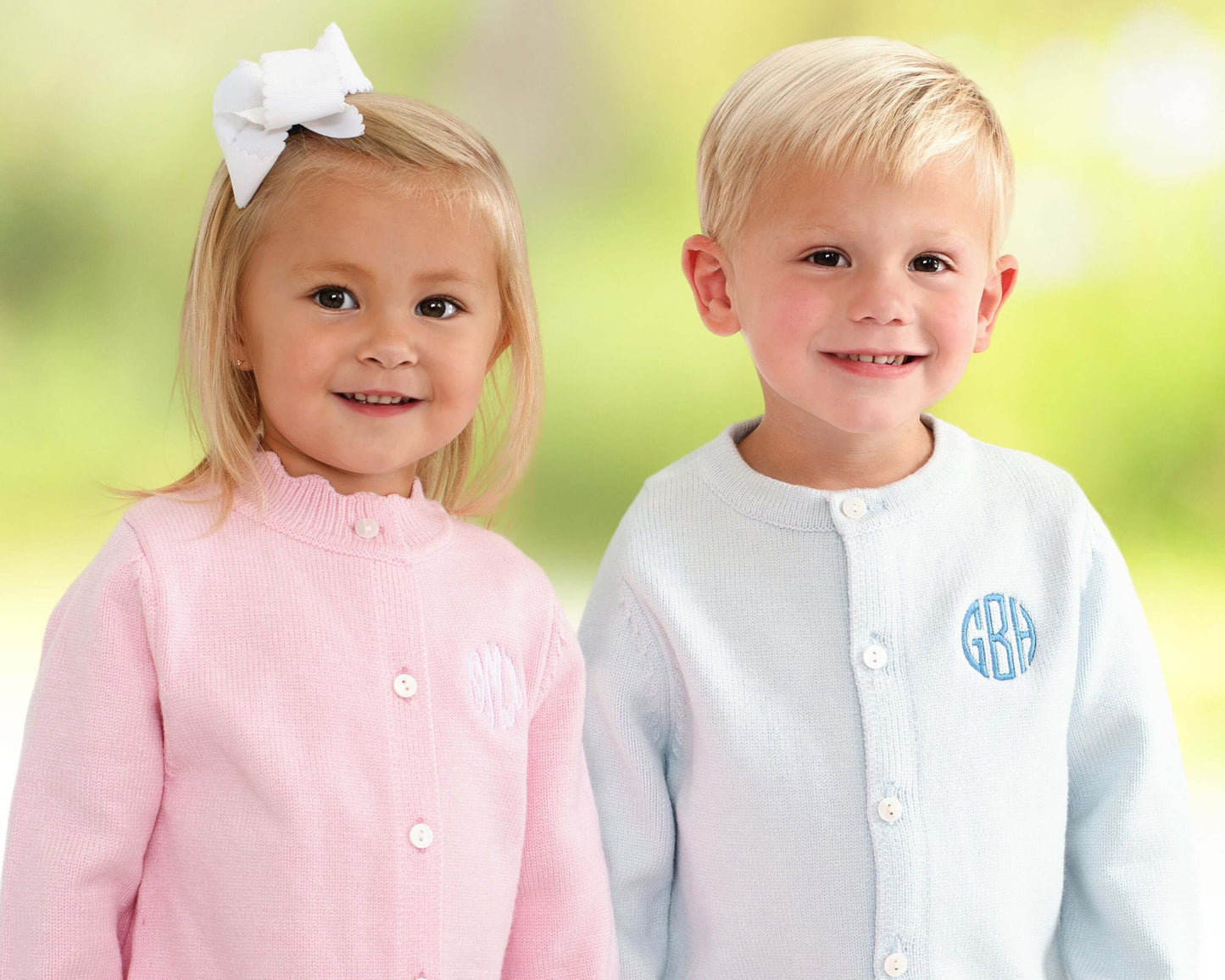 Two children wearing button-up shirts with monograms against a blurred green background