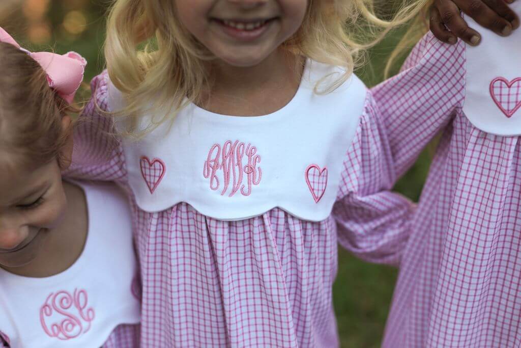Two children wearing matching dresses with monogram and heart designs.