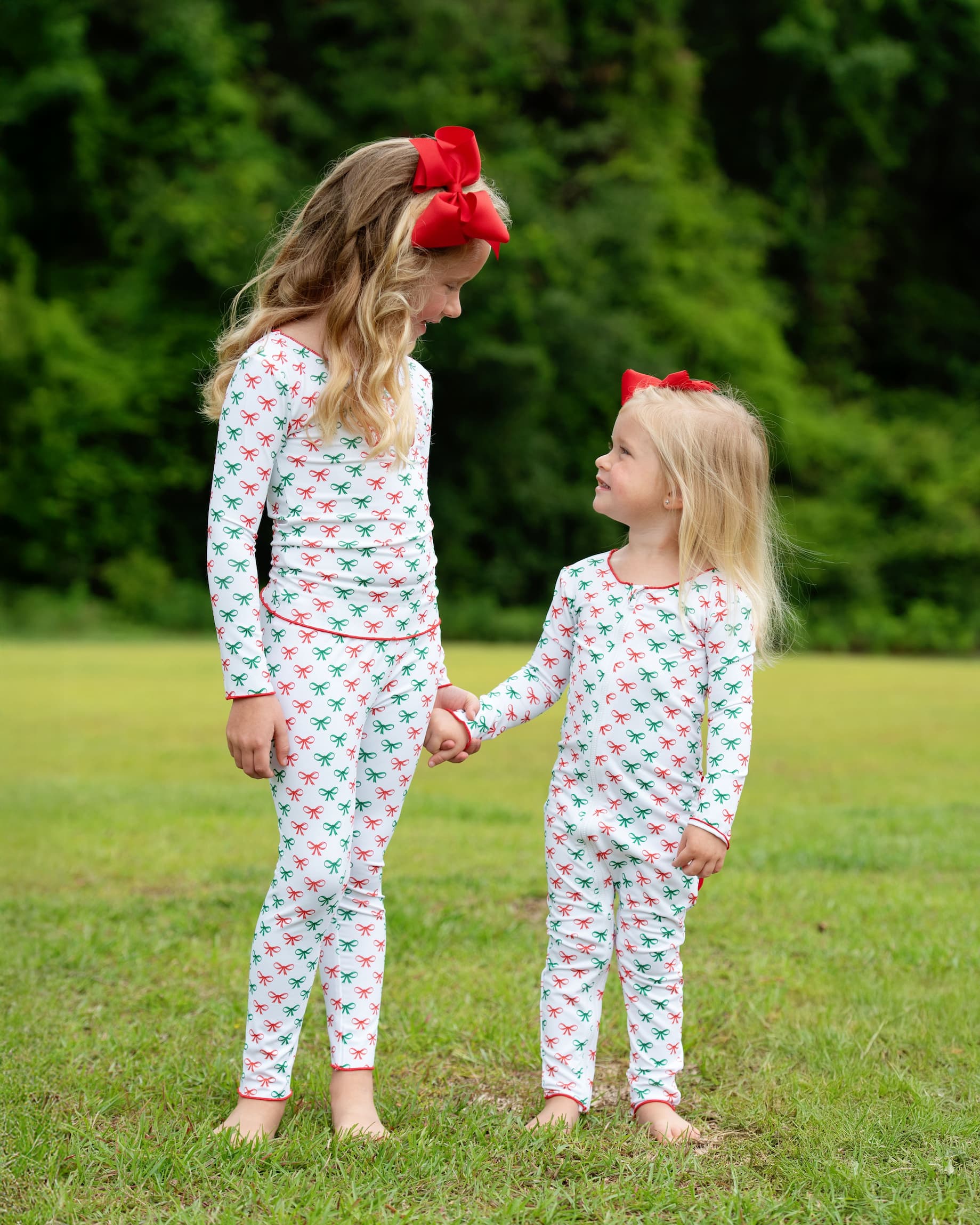 Two children wearing matching pajamas with a red and green pattern, standing in a grassy area.