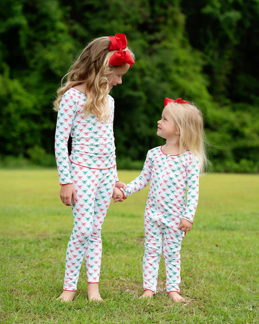 Two children wearing matching pajamas with a red and green pattern, standing in a grassy area.