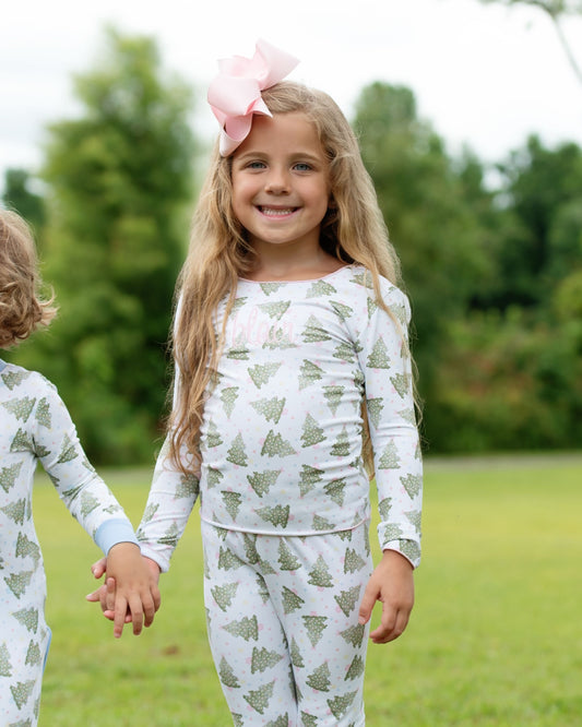 Two children wearing matching pajamas with a tree pattern outdoors.
