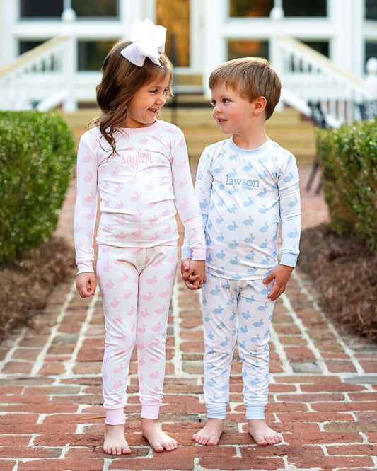 Two children wearing matching pajamas with embroidered names on a brick pathway.