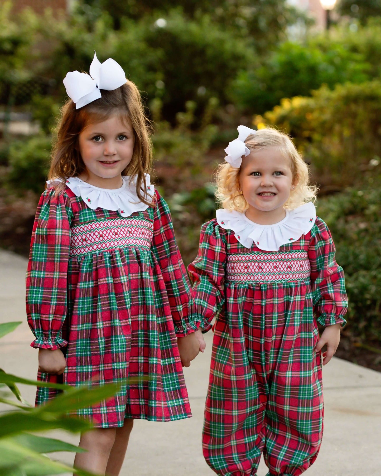 Two children wearing matching red and green plaid outfits with white collars outdoors.