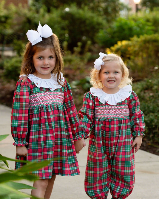 Two children wearing matching red and green plaid outfits with white collars outdoors.